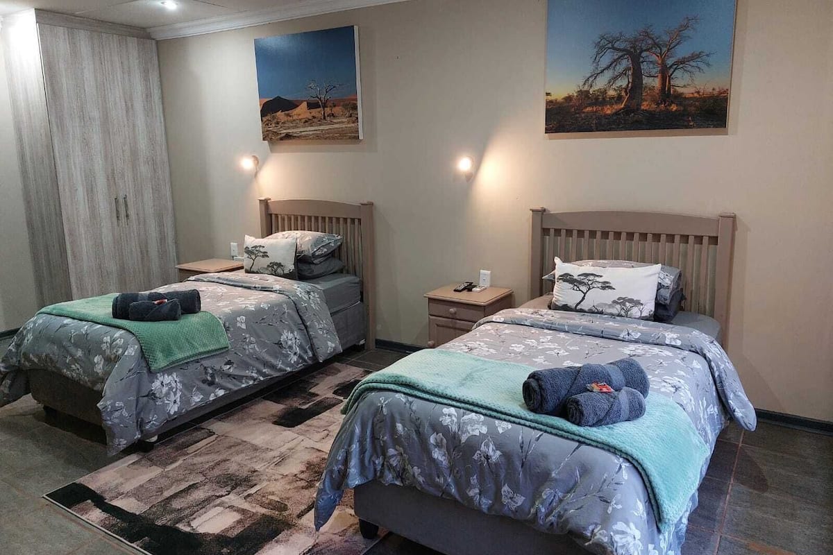 A bedroom with two beds, each with a wooden headboard, a nightstand, and a wall-mounted lamp.