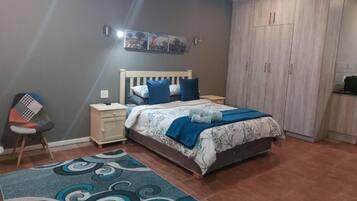 A bedroom with a bed, nightstands, a chair, a wardrobe, and a patterned rug.