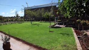 A well-maintained lawn with a paved walkway, a modern building in the background, and several potted plants. - Wisteria Lane Guesthouse (Tsantsabane)