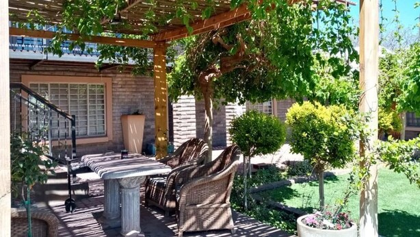 An outdoor patio with a pergola, wicker furniture, and a stone table. - Wisteria Lane Guesthouse (Tsantsabane)