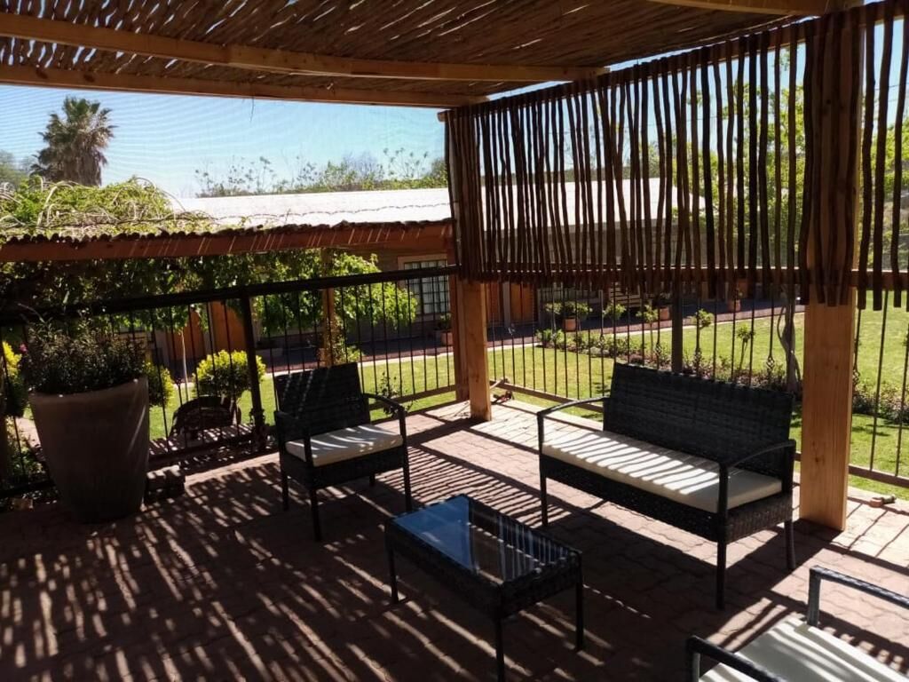 Um pátio externo com pérgola de madeira, dois bancos acolchoados e uma mesa pequena.