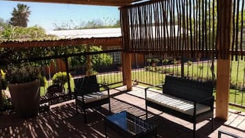 Um pátio externo com pérgola de madeira, dois bancos acolchoados e uma mesa pequena.