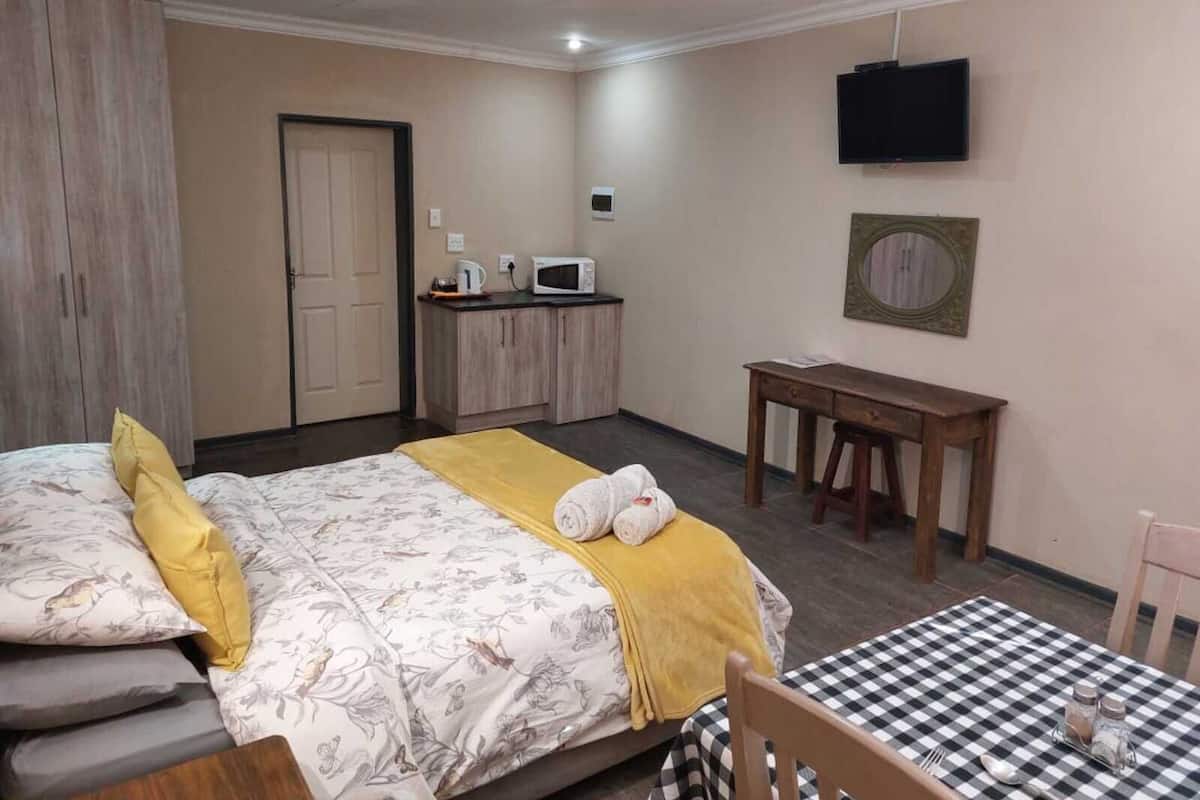 A bedroom with a bed, a desk, a chair, a table, a TV, and a wardrobe.