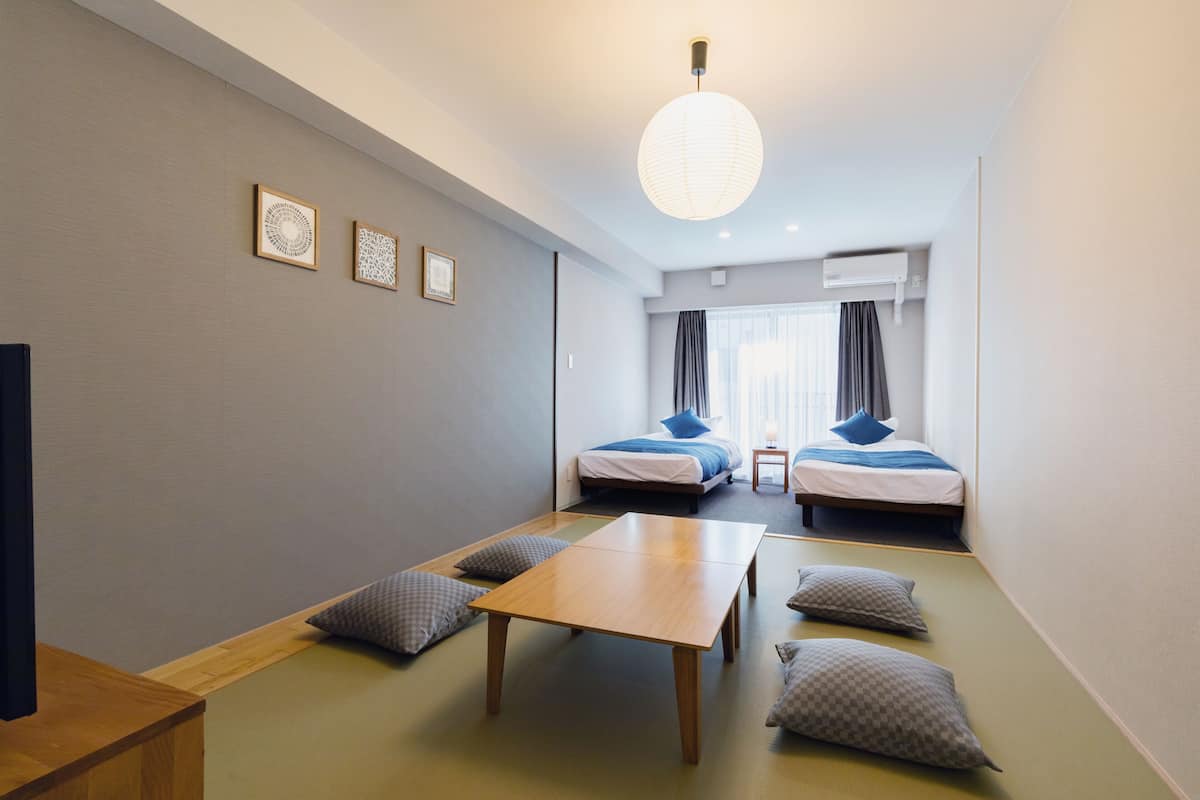 A modern hotel room with two beds, a wooden table, and tatami mats.