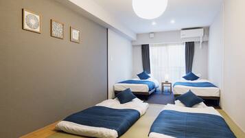 A hotel room with two single beds, a small table, and three framed artworks on the wall.