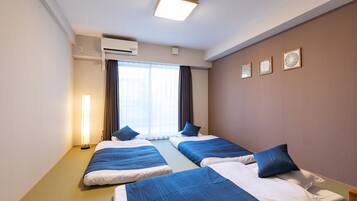 Une chambre d’hôtel avec deux lits, une fenêtre avec des rideaux, un appareil de climatisation et des œuvres d’art encadrées accrochées au mur.