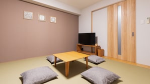 A room with a wooden table, four gray cushions, a television on a stand, and a sliding door. - HOTEL ECCLESIA (Kyoto)