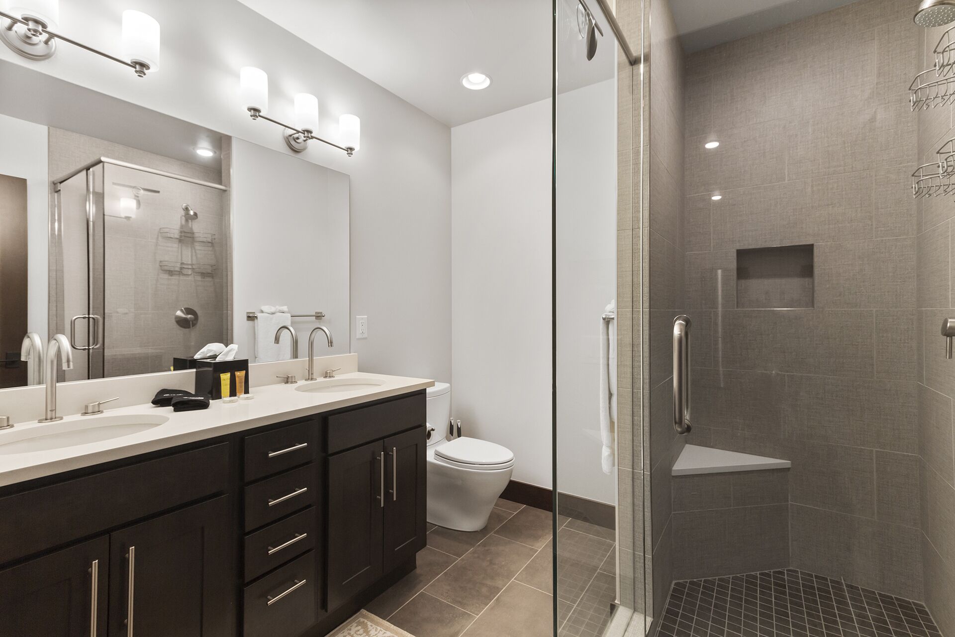 A modern bathroom with a glass-enclosed shower, a large mirror, and a vanity with dark cabinets and a white sink.