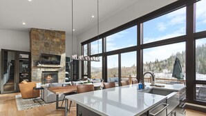 Une cuisine moderne dotée d’un grand îlot central, d’une cheminée en pierre et de larges fenêtres offrant une vue sur un paysage enneigé.