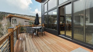 Une terrasse en bois avec des meubles d’extérieur, de grandes portes-fenêtres coulissantes et une vue sur un paysage montagneux.