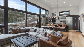 Un salon moderne avec un grand canapé d’angle, une table basse et une cheminée. La pièce est dotée de grandes fenêtres qui offrent une vue sur un paysage enneigé.