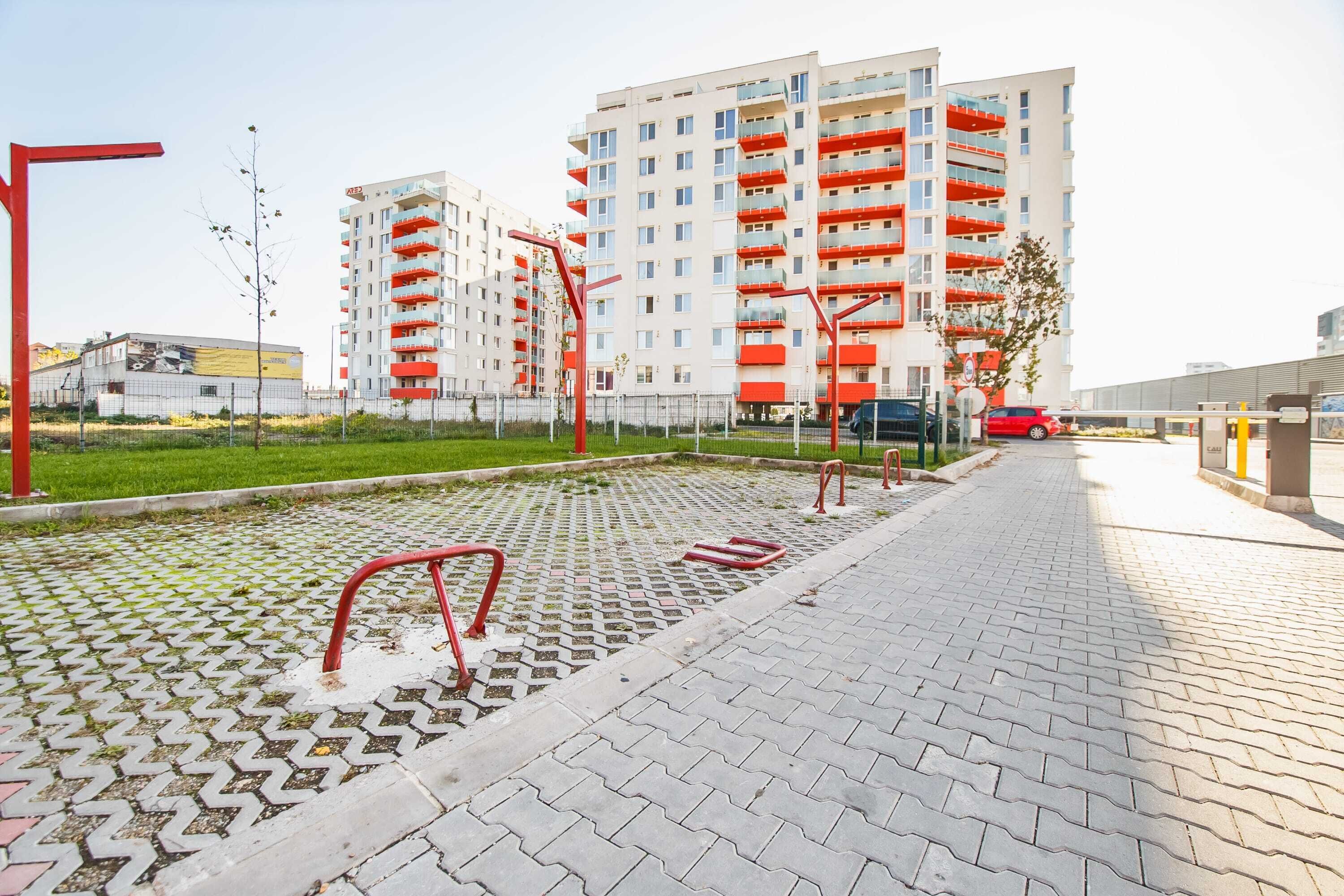 A modern apartment building with red balconies and a paved walkway with exercise equipment.