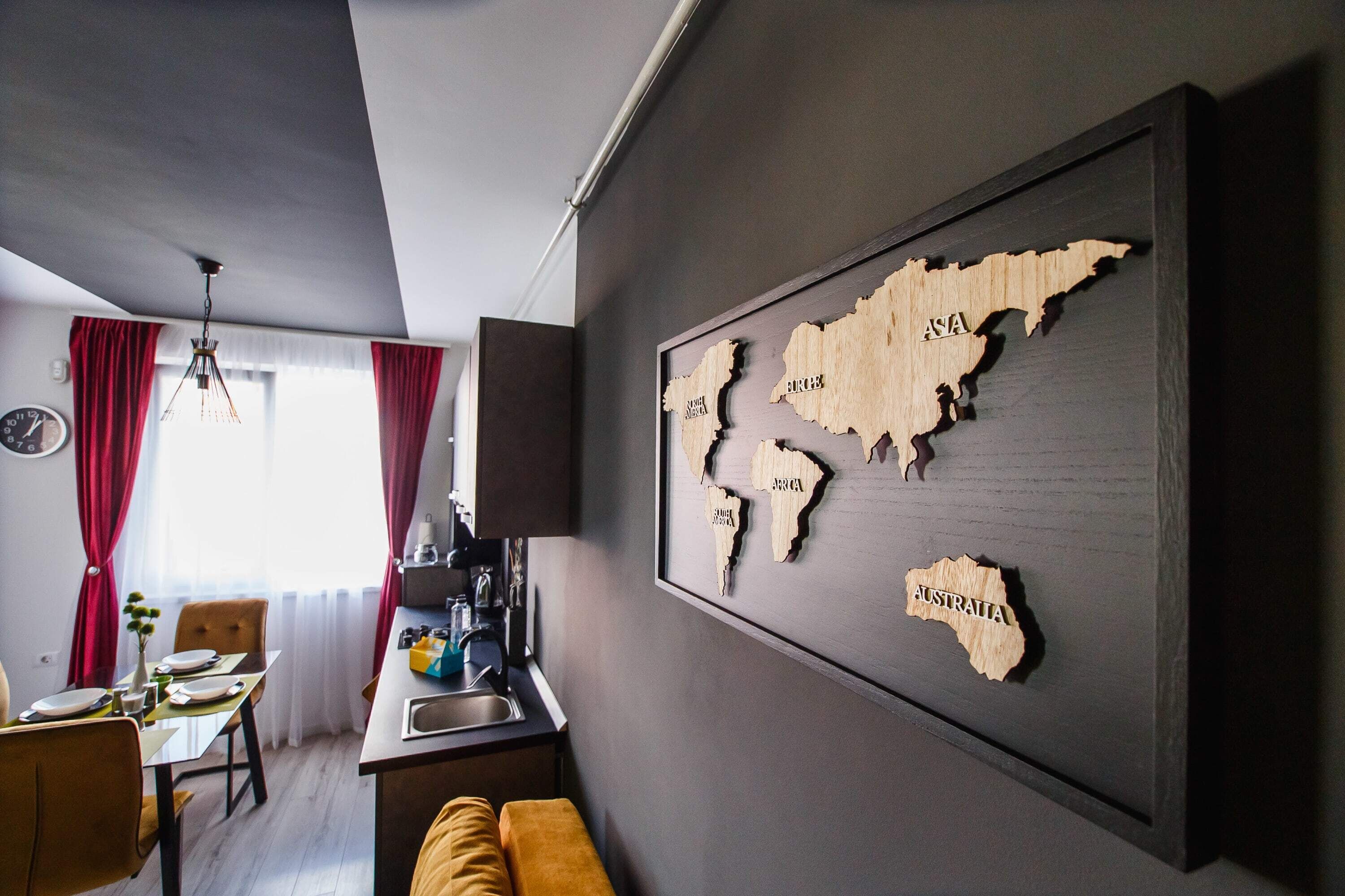 Una cocina moderna con comedor, un mapa del mundo en la pared y una ventana con cortinas rojas.