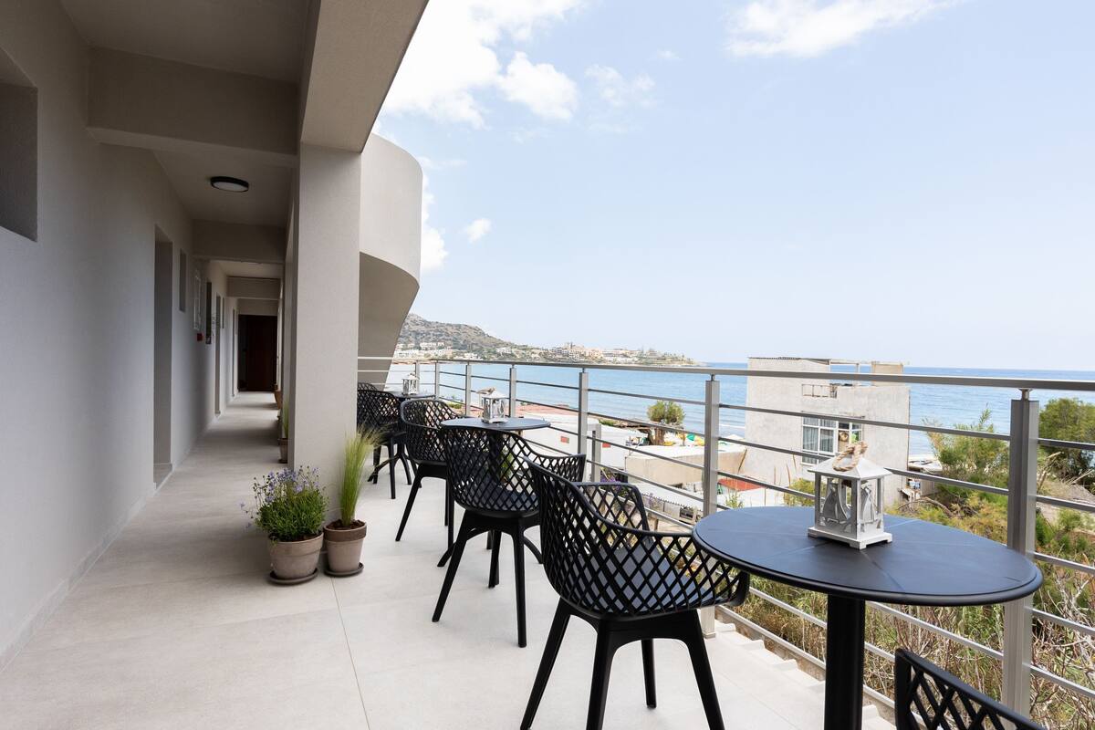 A balcony with outdoor seating, potted plants, and a view of the sea.