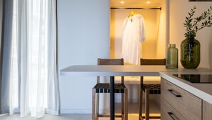 A modern room with a dining table, chairs, a hanging robe, and a vase with plants. - Niro Beachfront Living (Hersonissos)