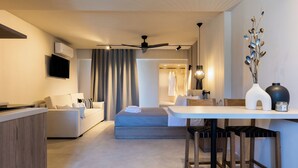 A modern hotel room with a sofa, a dining table with chairs, a ceiling fan, and a TV mounted on the wall. - Niro Beachfront Living (Hersonissos)