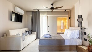 A modern hotel room with a bed, a sofa, a ceiling fan, an air conditioning unit, and a TV. - Niro Beachfront Living (Hersonissos)