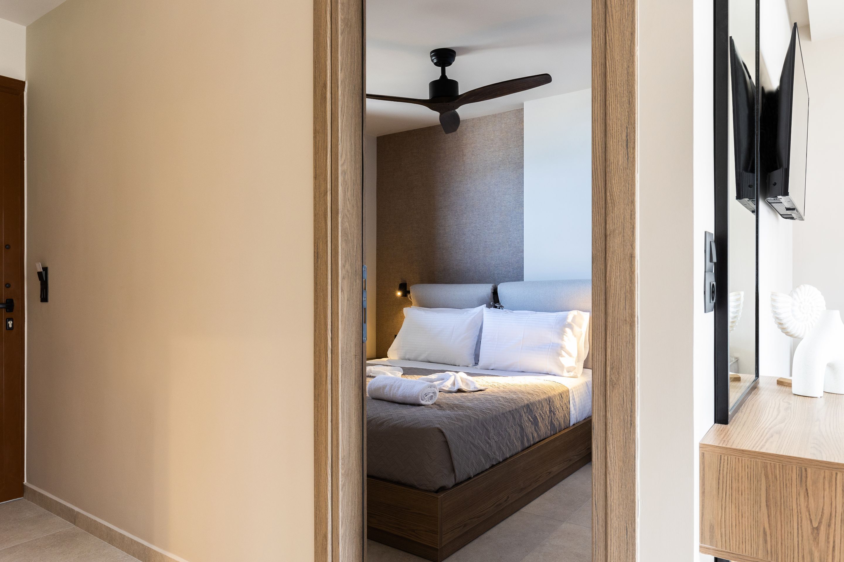 Een moderne slaapkamer met een houten bedframe, een plafondventilator en een nachtkastje met spiegel.