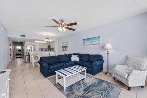 A living room with a blue sectional sofa, a white coffee table, a patterned rug, a white armchair, and a floor lamp.