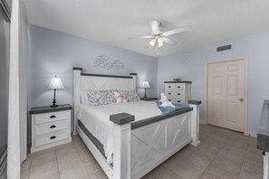 A bedroom with a bed, nightstands, a ceiling fan, a door, and a wall decoration.