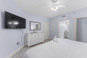 A bedroom with a bed, a dresser, a television mounted on the wall, and a ceiling fan.