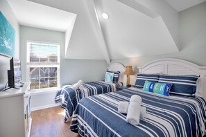 A bedroom with two beds, a window, and a desk with a computer.