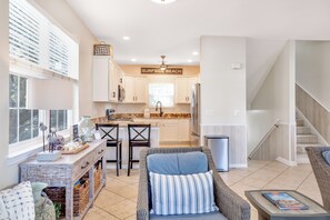 A spacious living area with a kitchen in the background, a wicker sofa, and a coffee table. - Z’s At The Sea | Surfside Beach 4BR Walk to Beach (Surfside Beach)