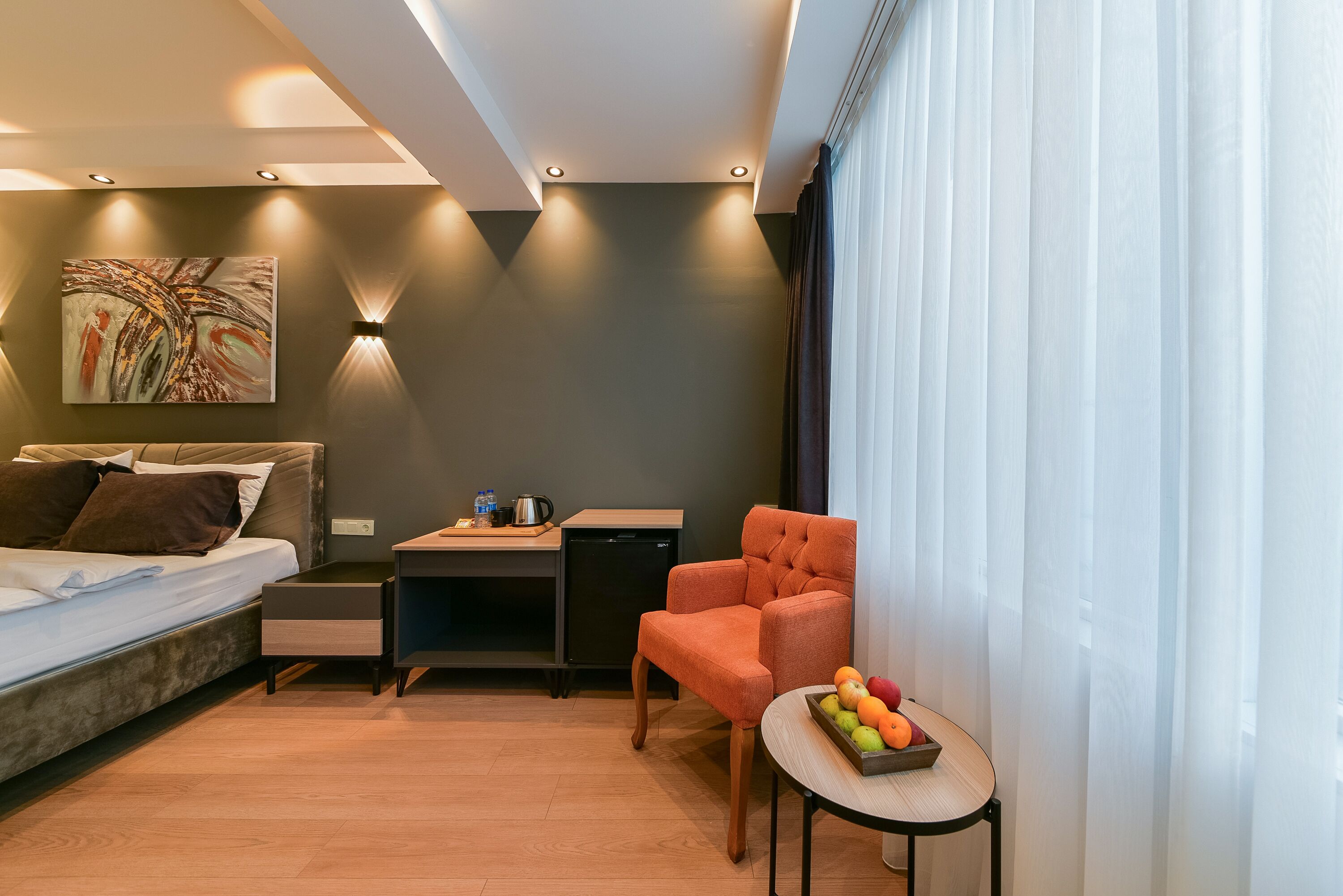 Una habitación de hotel moderna con cama, escritorio, silla y una pequeña mesa con fruta.