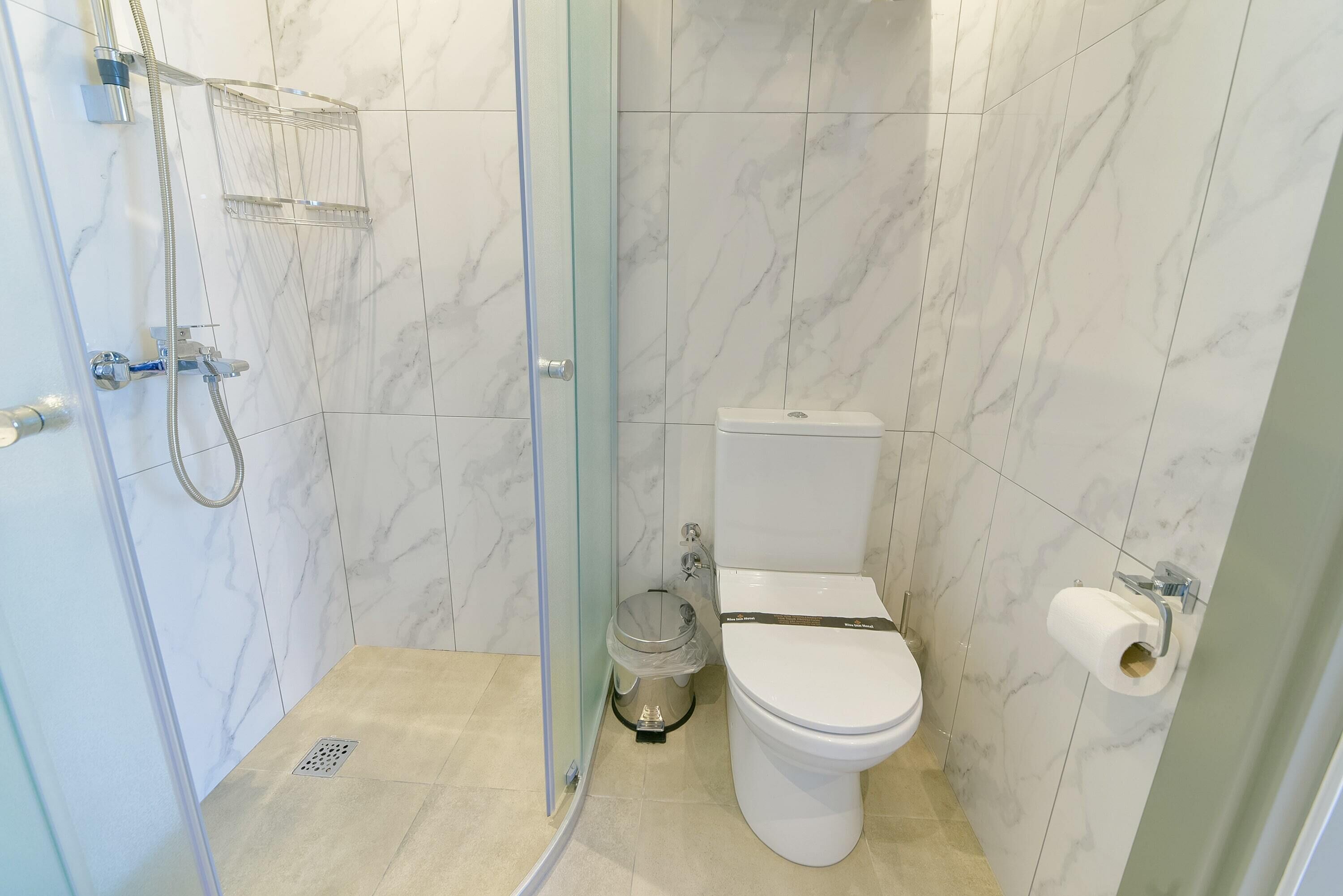 A bathroom with a glass-enclosed shower, a toilet, and a trash bin.