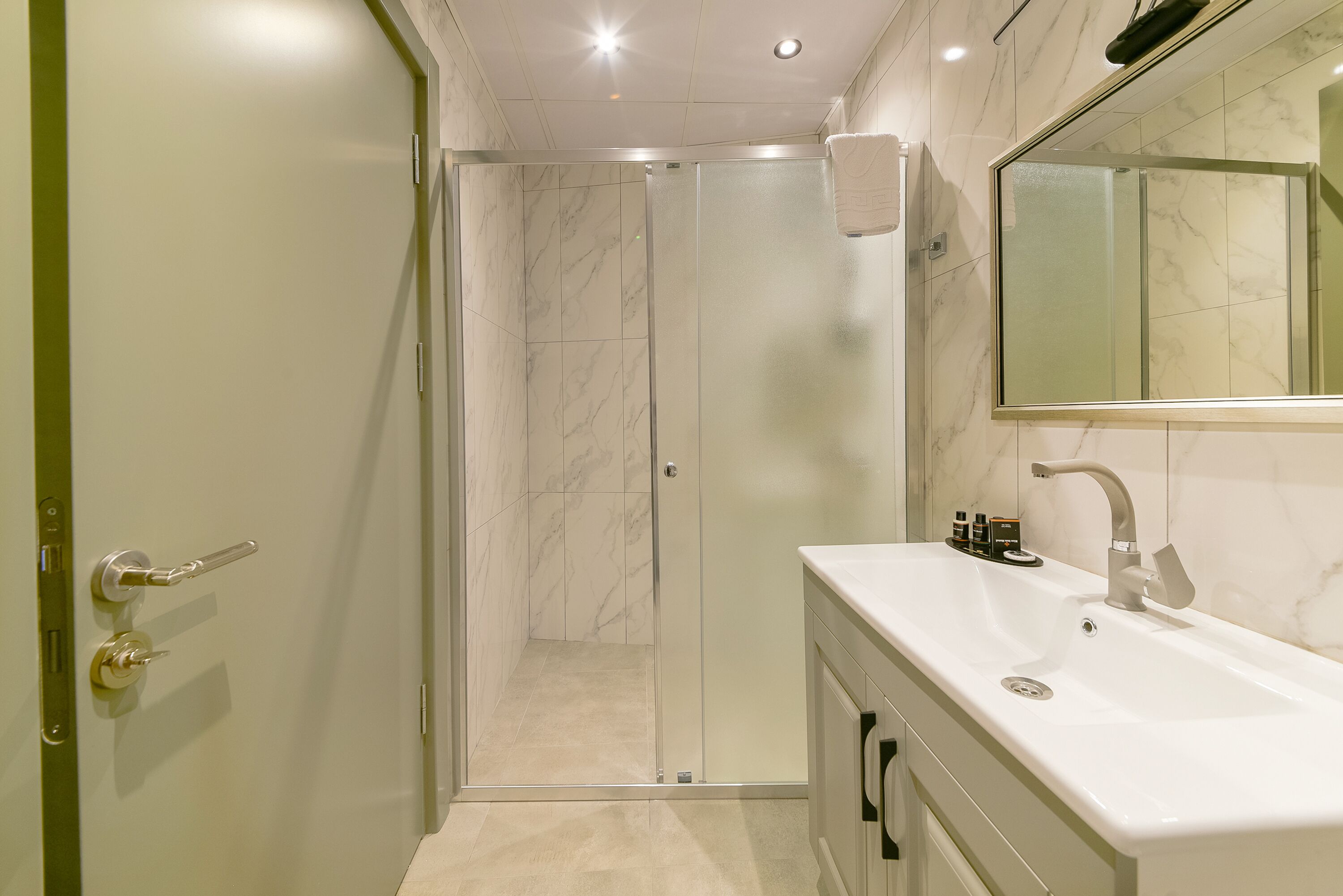 A modern bathroom with a glass-enclosed shower, a white sink, and a large mirror.