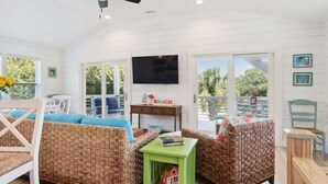 A room with wicker furniture, a green side table, a flat-screen TV, and a view of the outdoors.