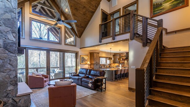 A spacious living area with a high ceiling, a wooden staircase, and a stone wall.