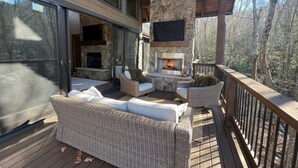 A deck with wicker furniture, a stone fireplace, and a TV mounted on the wall.