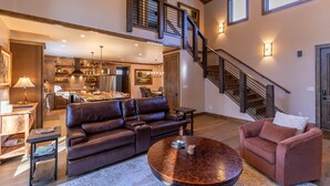 A spacious living area with a large brown leather sofa, a round coffee table, and a pink armchair. A staircase with wooden railings leads to an upper level.