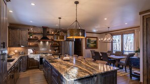 A spacious kitchen with granite countertops, stainless steel appliances, and a large island. There is a dining area with a table and chairs, and a large window providing a view of the outdoors.