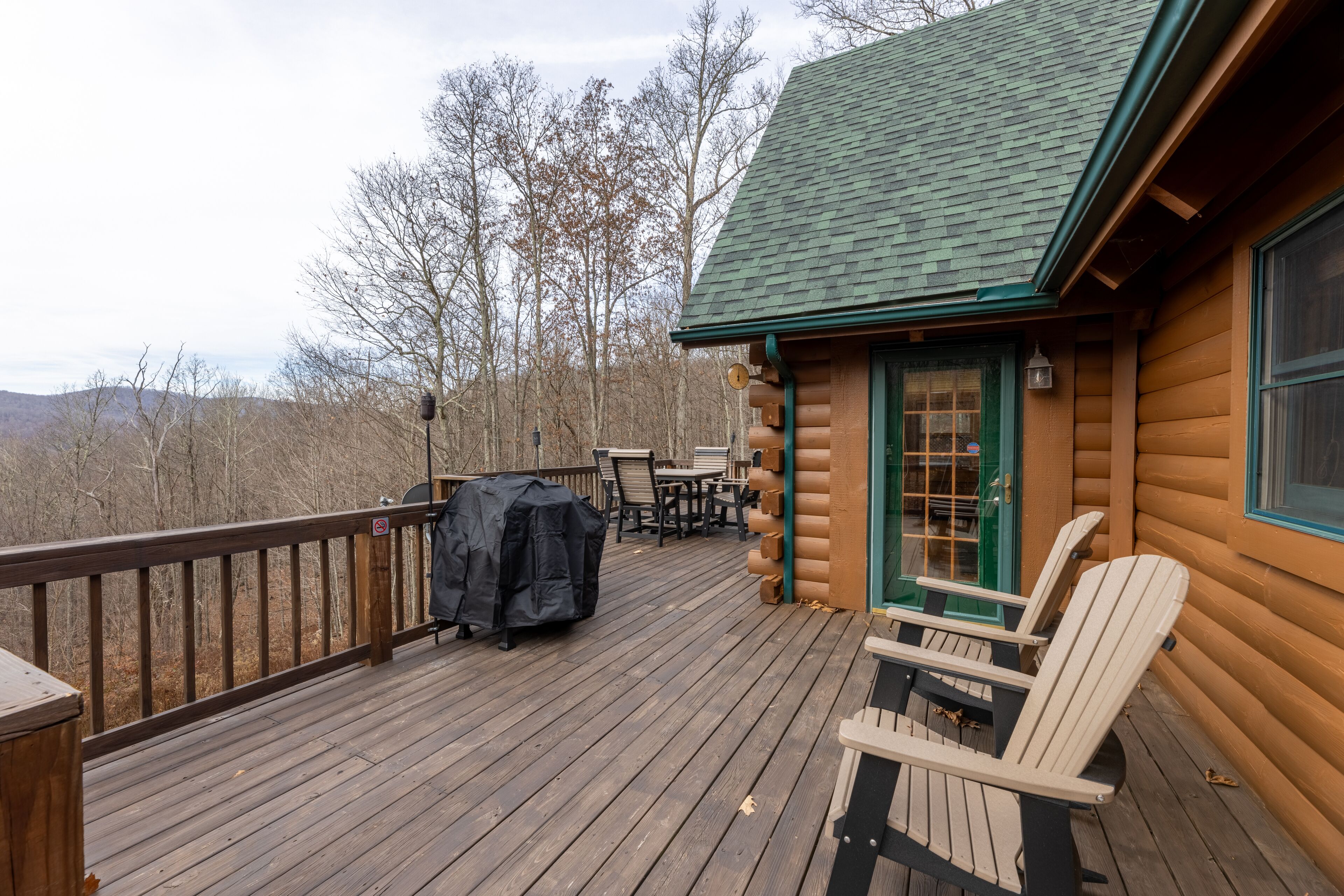 A log cabin with a deck, outdoor seating, and a covered grill area.