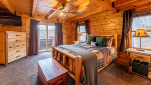 Quarto de cabana de toras com uma cama de madeira, um ventilador de teto, uma mesa de cabeceira, uma escrivaninha e um aparador.