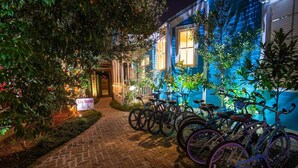 A nighttime view of a building with a 'Bike Rental' sign, a brick pathway, and several bicycles parked outside.