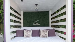 A cozy, enclosed sleeping area with a bed, a decorative wall with 'love Good Vibes' text, and two pillows with 'Good Vibes Only' text.