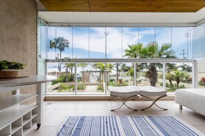 Une pièce moderne avec une grande fenêtre en verre, un canapé blanc, une petite table et un tapis à rayures bleues.
