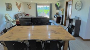 A dining area with a wooden table and chairs, a sofa, and a view of a green landscape through a glass door. - The Barndominium - Lots of Space! (Butternut)