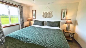 A bedroom with a large bed, two bedside lamps, a ceiling fan, and a view of the outdoors through a window. - The Barndominium - Lots of Space! (Butternut)