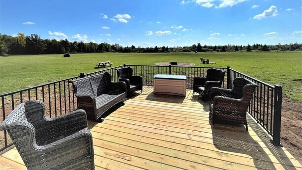 A deck with wicker furniture and a hot tub, surrounded by a metal railing, overlooking a grassy field. - The Barndominium - Lots of Space! (Butternut)