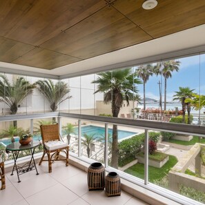 A balcony with a view of a pool and palm trees, wicker furniture, and decorative vases. - Wonder in Barra da Tijuca 3 Bedrooms Pp101 Z10 (Rio de Janeiro)