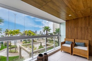 A balcony with wicker furniture and a view of a landscaped garden. - Wonder in Barra da Tijuca 3 Bedrooms Pp101 Z10 (Rio de Janeiro)