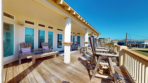 A wooden deck with outdoor seating, a covered area with windows, and a view of the surrounding buildings. - Absolute Paradise: 3 BR, 2 BA House in Crystal Beach , Sleeps 14 (Bolivar Peninsula)
