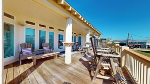 Une terrasse en bois avec des sièges extérieurs, un espace couvert avec des fenêtres et une vue sur les bâtiments environnants.