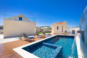 A modern outdoor swimming pool area with lounge chairs and a clear blue sky. - Villa Makisland (Chania)