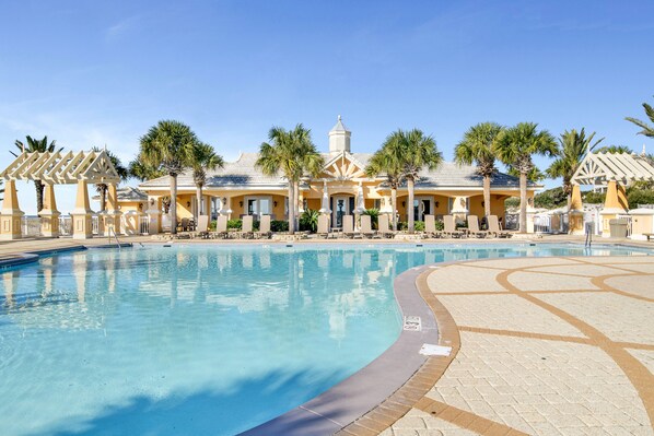 A large pool with a tiled deck, surrounded by palm trees and a building with multiple balconies.