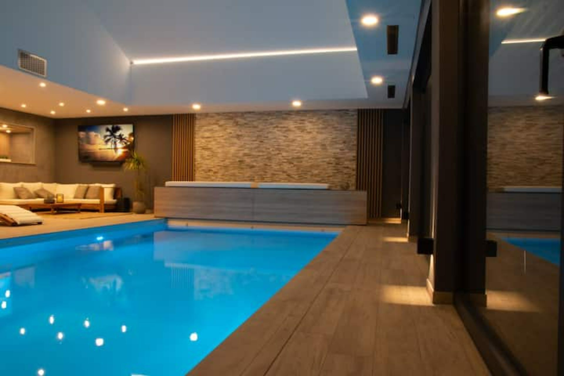 An indoor swimming pool with a wooden deck, a sofa, and a stone wall.